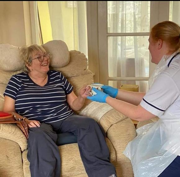 Carer giving lady a cup of tea on social visit