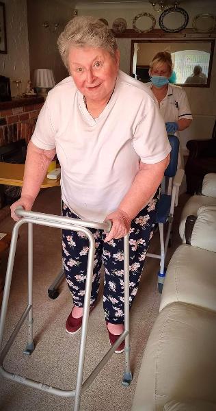 elderly lady with walking frame. care assistant behind with wheel chair